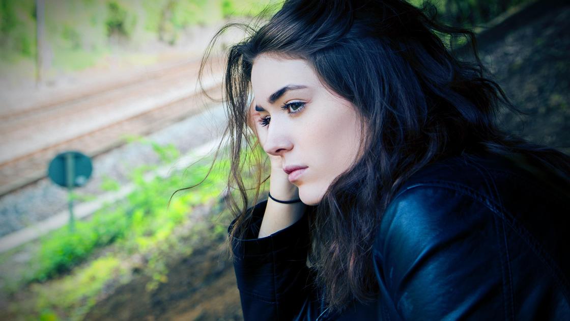 Темноволоса дівчина в чорній куртці сумно дивиться в далечінь Темноволосая девушка в черной куртке грустно смотрит вдаль