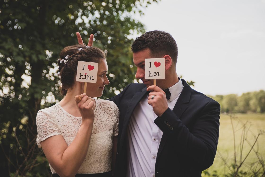 Чоловік і жінка стоять, обійнявшись і закриваючи обличчя табличками з освідченням у коханні Мужчина и женщина стоят, обнявшись и закрывая лица табличками с признанием в любви