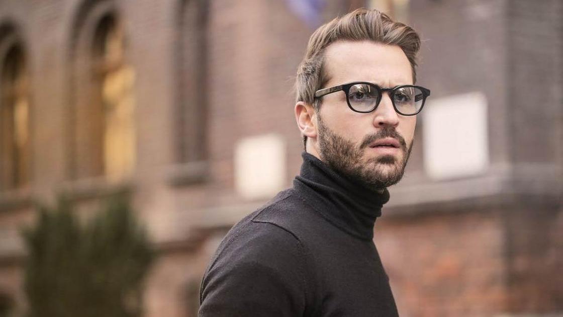 Чоловік в окулярах і темний светр на міських вулицях фону Мужчина в очках и темном свитере на фоне городских улиц