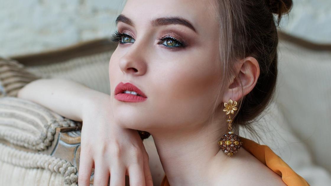 Дівчина з красивий вечірній макіяж сидить на дивані Девушка с красивым вечерним макияжем сидит на диване