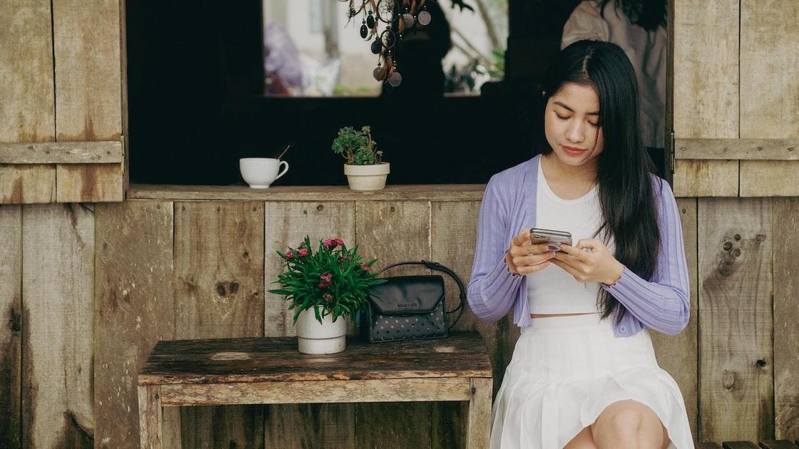 Дівчина пише повідомлення, сидячи за столиком на вулиці Девушка пишет сообщение, сидя за столиком на улице